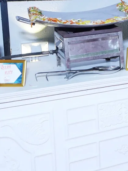 A close-up of one of my live cooking stations. This setup includes a large pan for dishes like Paneer Tava Masala, alongside labeled chafing dishes for Jeera Rice and Chicken Tikka Masala.