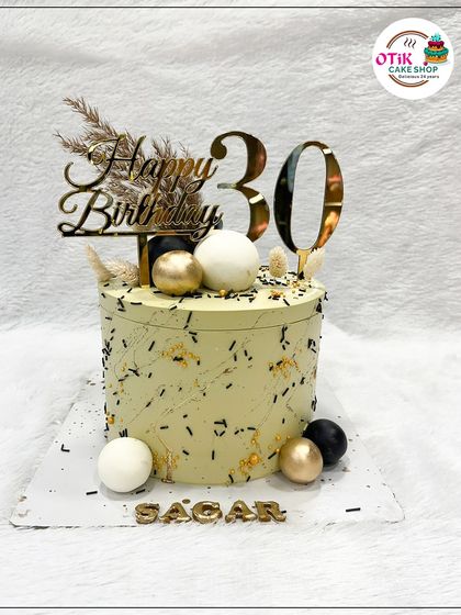 A chic and modern cake for a 30th birthday celebration. The pale green buttercream is speckled with black, and the cake is decorated with black, white, and gold spheres and dried botanicals.