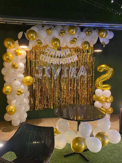 A second birthday party with a classic white and gold theme, featuring a balloon arch and shimmer curtain.