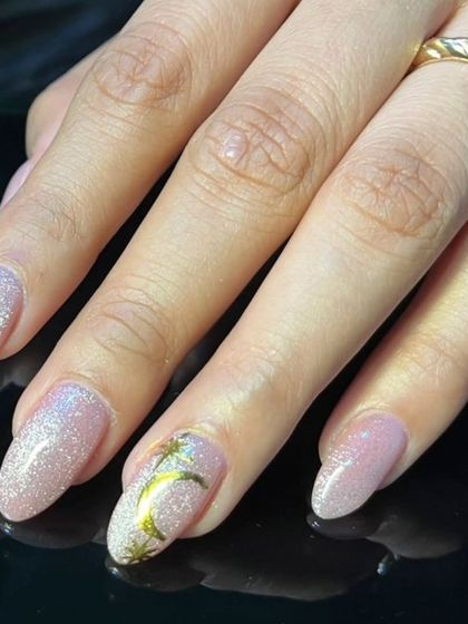 A beautiful manicure featuring soft pink glitter nails with a celestial gold moon and star accent.