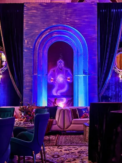 For the "Genie Glow" section of the party, I created this mystical lounge area with a glowing Genie backdrop, deep blue velvet curtains, and plush seating.