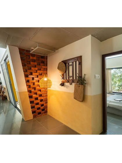 The entrance corridor of Aamra, where a wall of projecting bricks creates a dynamic play of light and shadow. The half-painted wall in yellow oxide introduces warmth and guides the eye towards the living spaces beyond.