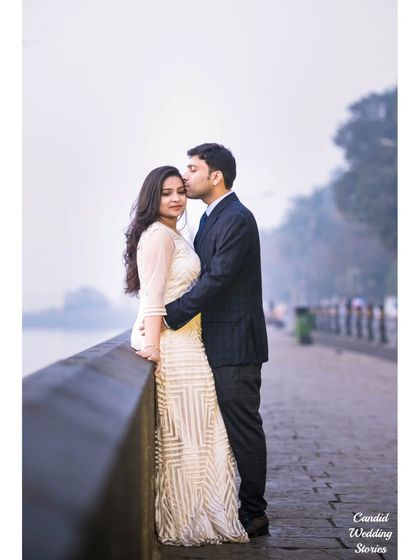 A tender forehead kiss on a quiet promenade, with the hazy Mumbai skyline in the distance, creating a soft and romantic mood.