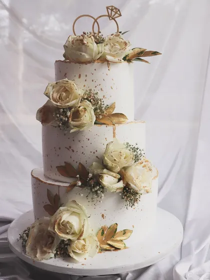 A classic three-tier wedding cake that never goes out of style. This design features delicate gold speckles, a subtle drip effect, and is adorned with beautiful white roses and baby's breath for a timeless and elegant feel.