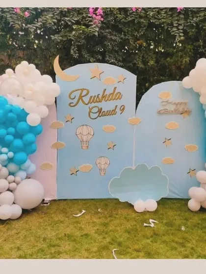 A dreamy 'Cloud 9' themed outdoor birthday setup. This decoration uses custom backdrops and balloon clouds in shades of blue, grey, and white to create a heavenly atmosphere.