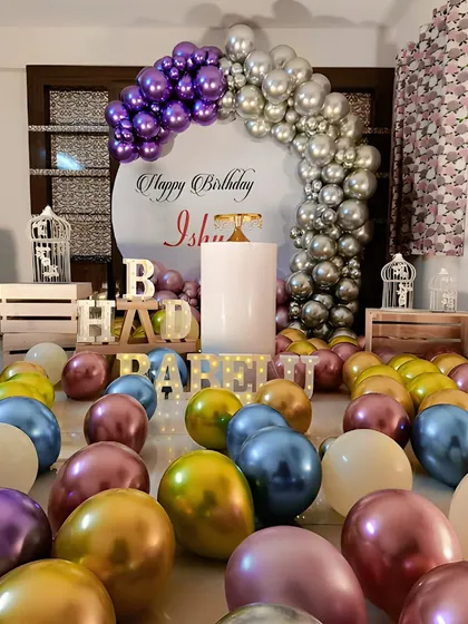 A chic and simple home birthday decoration. This setup features a half-arch of purple and silver chrome balloons against a circular backdrop, with dozens of colorful balloons scattered on the floor for a fun, immersive feel.