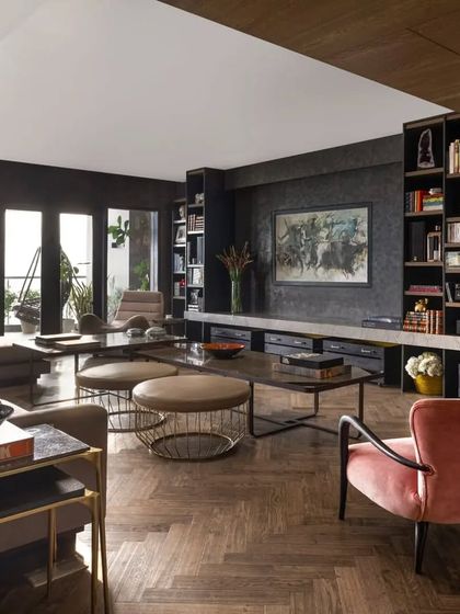 A view of the living room in the Caitriona apartment, highlighting the custom-built bookcase and media unit. The space is designed for a young professional, blending high-tech features like a retractable screen with personal touches and comfortable, stylish furniture.