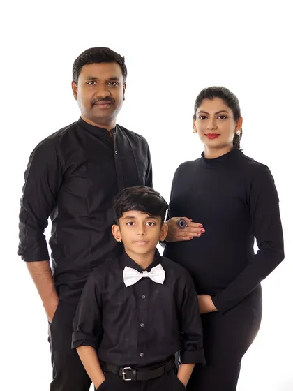 A chic and timeless family maternity portrait. The coordinated black outfits create a sophisticated look against a simple background, focusing on the family's connection.