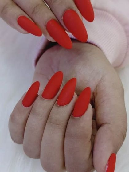 A side view of the long, matte red almond nails, showing their elegant shape.
