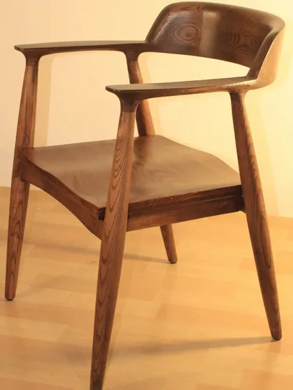 The distinctive grain of the ash wood is the highlight of this dining chair. The armrests are sculpted to flow seamlessly from the backrest, a detail that requires precise craftsmanship.