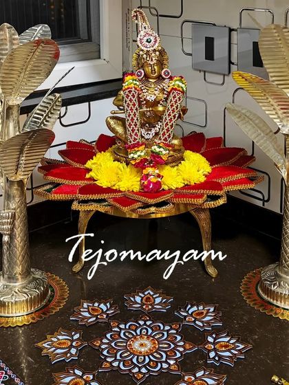 A pooja setup in a new home, with a goddess idol placed on a lotus-themed stand, flanked by brass banana tree props.