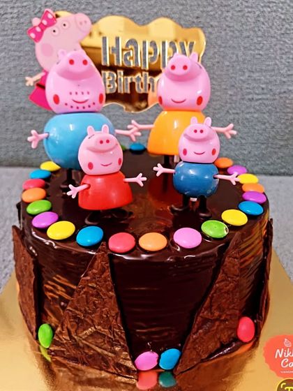 This is a fun chocolate version of the Peppa Pig theme cake. It features a rich chocolate ganache, a chocolate shard border, and colorful gems, along with the adorable Peppa Pig family toppers.
