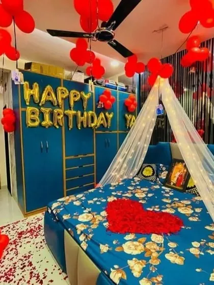 A beautiful birthday surprise for your loved one. This bedroom decoration includes red balloons, a heart made of rose petals on the bed, a light-up canopy, and "Happy Birthday" foil letters.