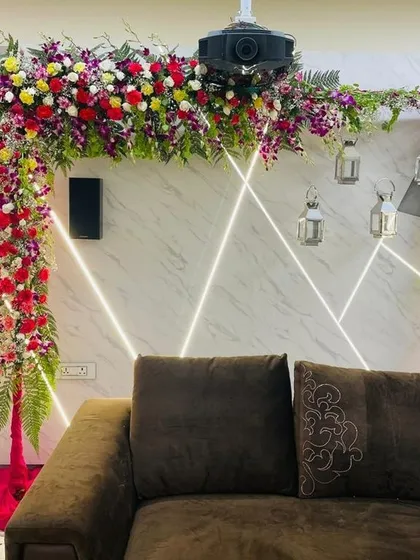 A colourful L-shaped floral arch set up indoors over a sofa. This arrangement uses a mix of orchids, roses, and ferns to create a lush, garden-like feel inside your home.