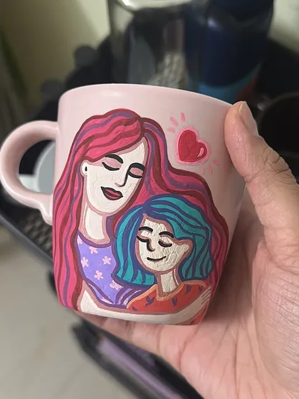 A sweet, stylized illustration of a mother and daughter hugging, painted on a pink mug.