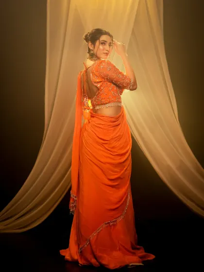 A full-length shot showcasing the back detail of an orange designer saree. In the studio, I can precisely light every element to ensure the garment's craftsmanship is clearly visible.