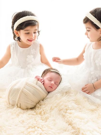Twin sisters curiously watch over their sleeping baby sister. This image captures the wonder and sweetness of a growing family.