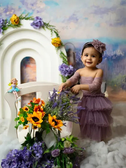 This little girl's smile is as bright as the sunflowers in her photoshoot. The combination of purple and yellow creates a vibrant and cheerful scene.