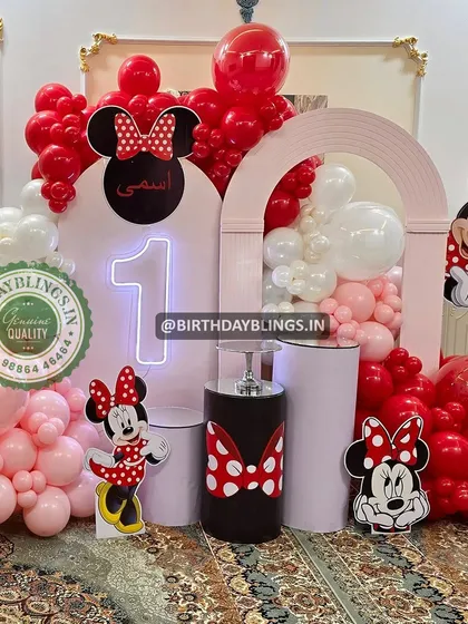 A classic Minnie Mouse first birthday in her signature red, white, and pink. The setup features multiple cutouts, a neon number '1', and themed plinths.