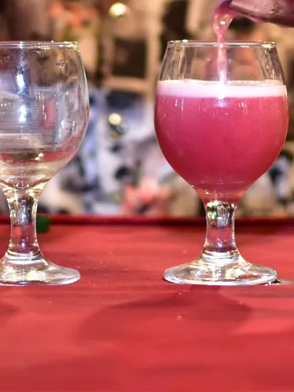 The final pour of a colorful, freshly shaken cocktail into a wine glass. The vibrant pink hue makes it an attractive option for guests.