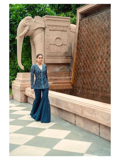 Sharvari walking towards the camera, with a beautiful fountain and elephant sculpture in the background. A shot that feels both grand and graceful.