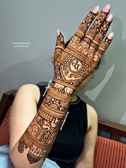 A beautiful bride showing her full-arm back-of-hand mehndi. The design is personalized with the initials "DP" and features a rich tapestry of traditional motifs.