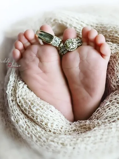 A classic newborn detail shot, focusing on the baby's tiny feet held in a soft wrap, adorned with their parents' wedding rings. It’s these little details that you will cherish forever.