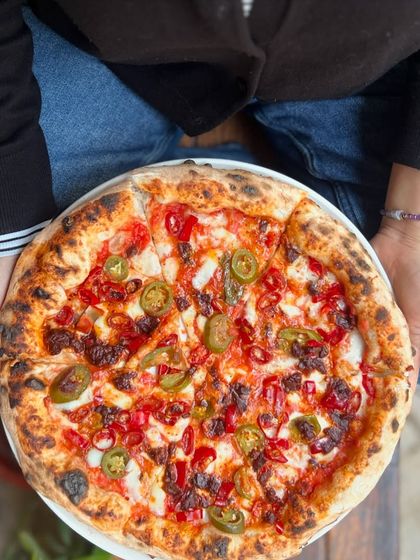 Holding a freshly baked spicy pizza. It's the perfect size for one, if you're brave enough.