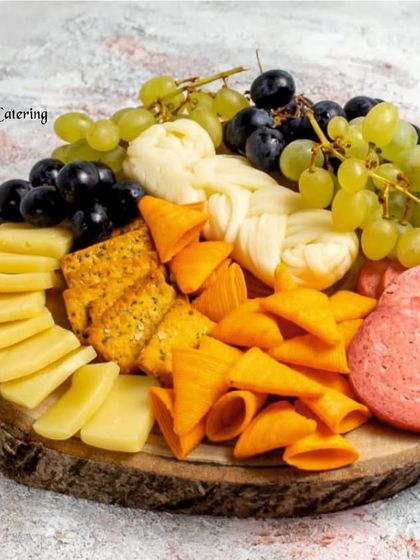 A rustic wooden platter featuring a mix of cheeses, cured salami, cone-shaped crackers, and fresh grapes. This board is perfect for a casual yet gourmet gathering.