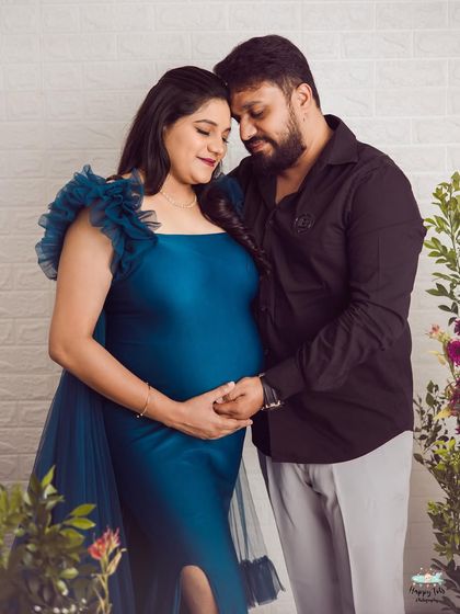 An intimate portrait showing the couple holding hands over the baby bump. The deep teal gown adds a touch of richness to this loving moment.