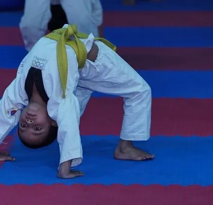 Even our youngest students begin flexibility training early. A young boy in his dobok and yellow belt holds a perfect back bridge, building a strong foundation for future skills.