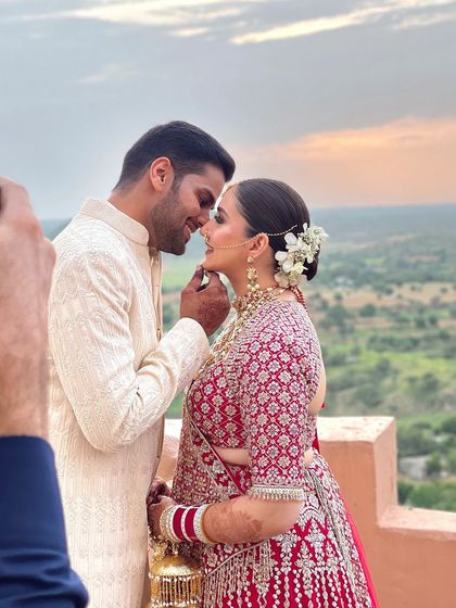 A romantic shot of the couple. The bride's floral bun adds a soft, delicate touch to her powerful red bridal lehenga.