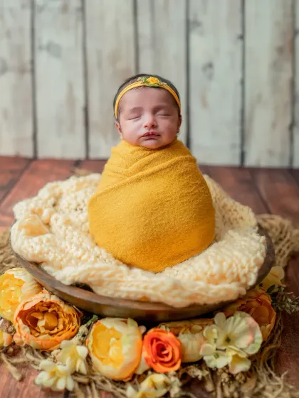 A classic bowl pose with the baby swaddled snugly in a vibrant yellow wrap, surrounded by matching flowers.
