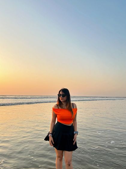 A full-length shot of my orange top and black skirt from NewMe at the beach. This is a great example of a simple but stylish sunset outfit.