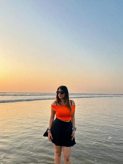 A full-length shot of my orange top and black skirt from NewMe at the beach. This is a great example of a simple but stylish sunset outfit.