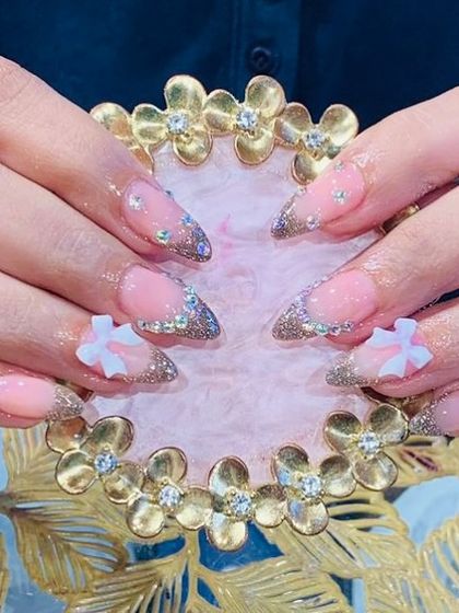 A glamorous set of extensions with a glittery French tip, rhinestone details, and 3D white bows.