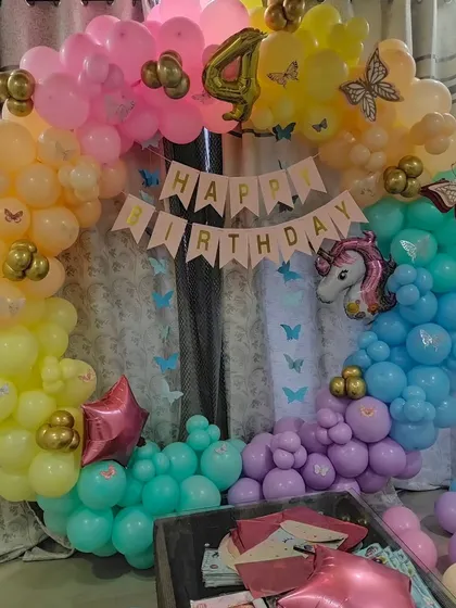 A rainbow-colored balloon arch with unicorn and butterfly details for a 4th birthday party.