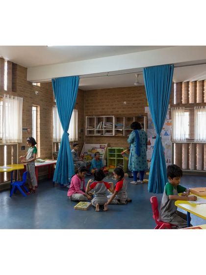 A classroom at Buddhi School where flexible blue curtains divide the space for different activities. The vertical fins on the windows diffuse sunlight, creating an ideal, glare-free atmosphere for learning.
