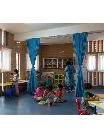 A classroom at Buddhi School where flexible blue curtains divide the space for different activities. The vertical fins on the windows diffuse sunlight, creating an ideal, glare-free atmosphere for learning.