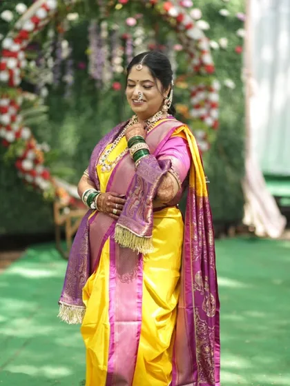 This bride looks absolutely regal in her yellow and purple Paithani saree. Her makeup is balanced to harmonize with the vibrant colors of her attire and the outdoor wedding decor.