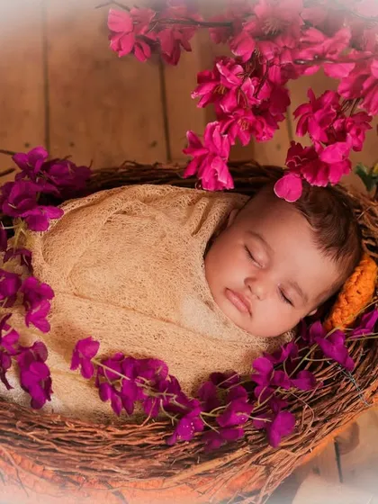 A newborn sleeps peacefully in a rustic nest adorned with beautiful pink flowers. The soft, dreamy filter adds to the magical quality of the portrait.