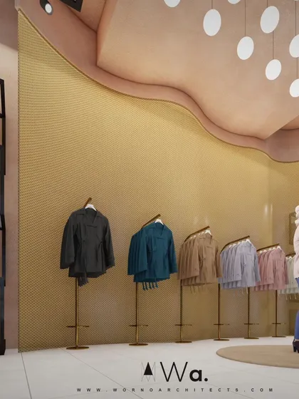 A detail of the apparel store showing a curved, textured feature wall in a golden-yellow hue. This element adds a soft, organic shape to the space and serves as an elegant backdrop for minimalist clothing racks.