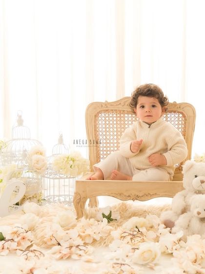 A classic first birthday portrait. The "One" sign, teddy bears, and a floor covered in white flowers create a beautiful and timeless setting for this little boy's celebration.