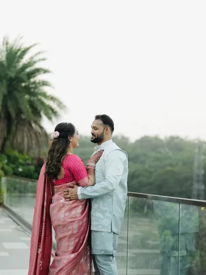 A wide shot of the couple against a scenic background, showcasing the bride's elegant saree and hairstyle.