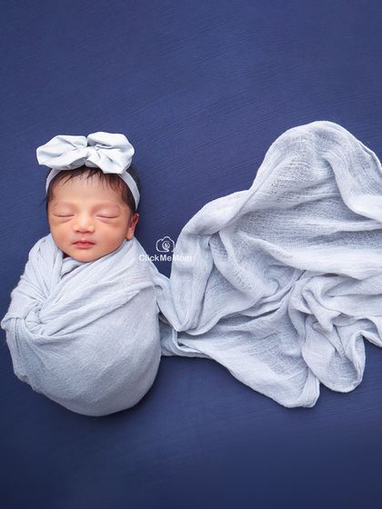 A minimalist portrait focusing on color and texture. The baby is wrapped in a soft gray swaddle against a deep blue background, with the fabric elegantly draped.