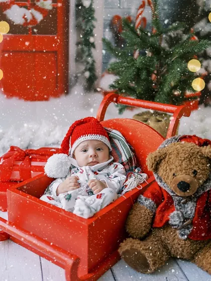 A peaceful newborn nestled in a red sleigh, celebrating his very first Christmas.
