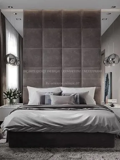 A contemporary bedroom with a tall, grid-tufted headboard in a dark grey fabric. The mirrored side panels and sleek pendant lights enhance the room's modern aesthetic.