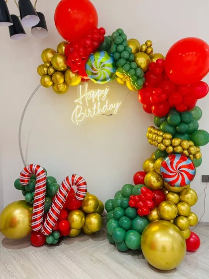 A festive Christmas-themed birthday decoration. The balloon ring features red, green, and gold colors with candy cane foil balloons.