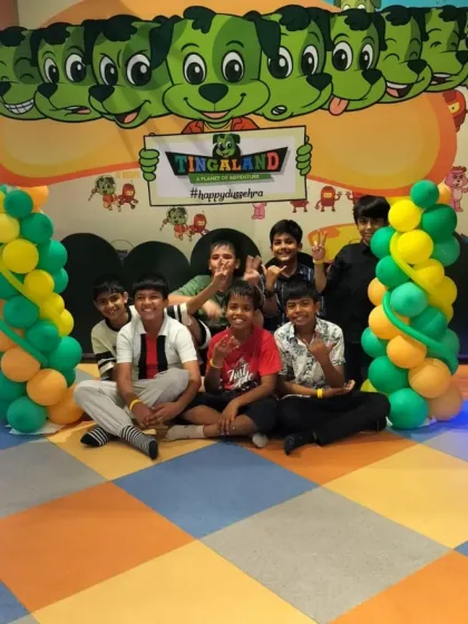 A group of boys poses between balloon columns with our mascots in the background, celebrating a fun day at our Noida location.