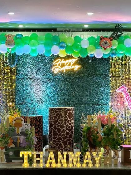 A jungle party stage with a green hedge backdrop and a gold shimmer panel. The scene is brought to life with various animal cutouts, a light-up number '1', and a personalized name sign.